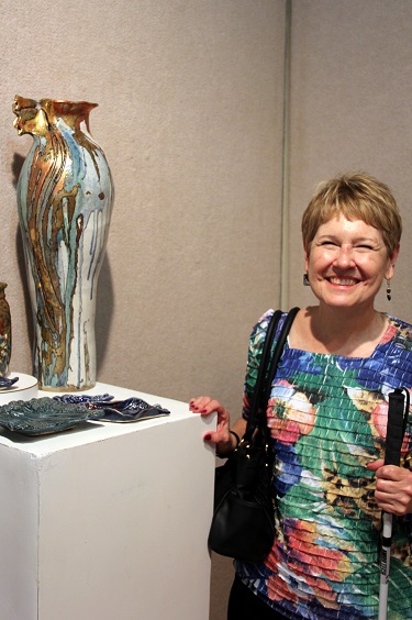Lynda wearing earrings and standing next to blue vase
