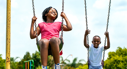 A girl and boy swinging, big smiles on their faces