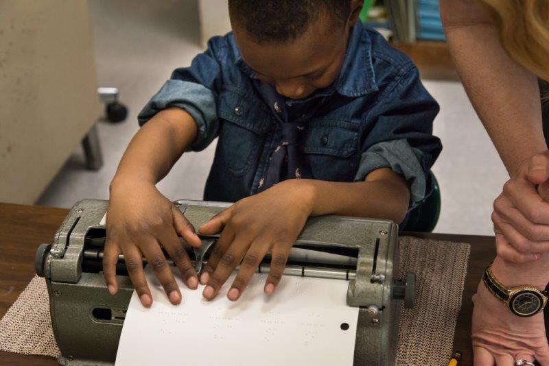 boy leaning over braillewriter