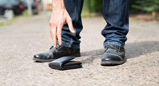 man reaching for fallen wallet on the sidewalk