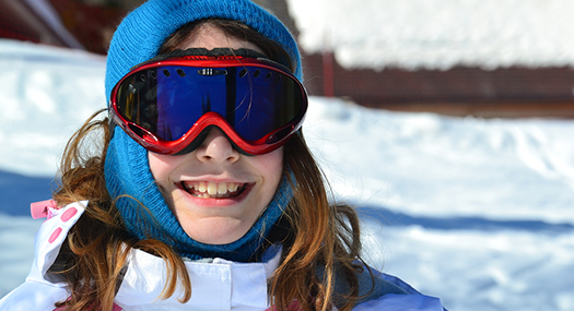 Young girl smiling, wearing protective snow goggles on a ski slope