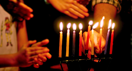 hands of family members around a lit Menorah