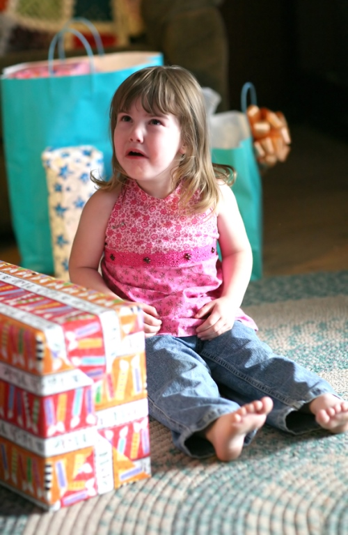 A young girl sits surrounded by gifts. She is crying.