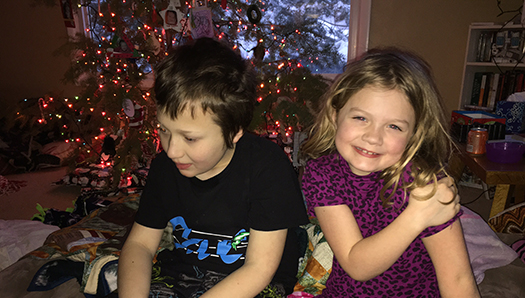 Eddie and his sister CC sitting in front of a decorated Christmas tree