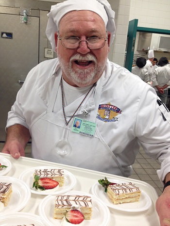 Joel wearing chef's hat ad holding tray of pastries with strawberries 