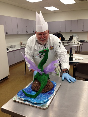 joel wearing chef's hat and leaning over centerpiece with dragon