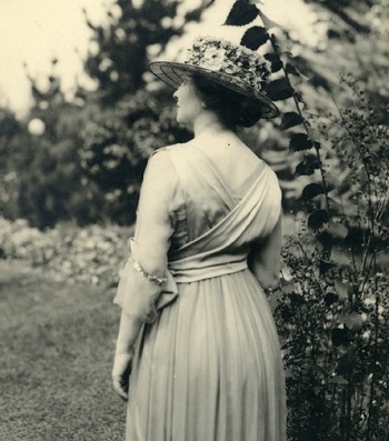 Helen wearing hat and long dress standing in garden