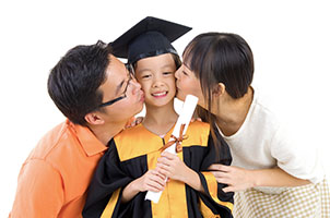 Kindergarten child in graduation gown and mortarboard kissed by her parents during graduation