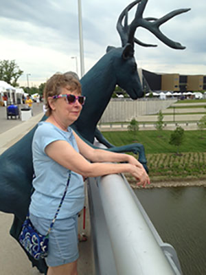 Mary Hiland standing on a bridge next to a deer statue looking out