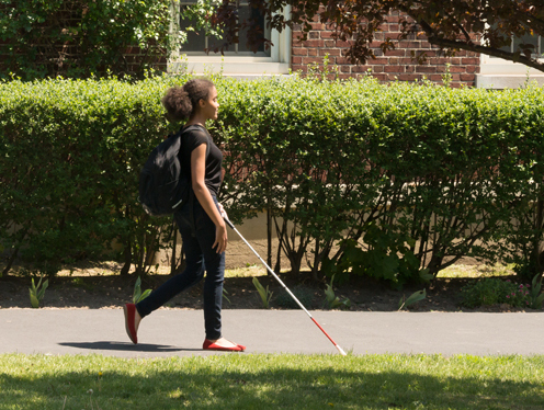 Teenage girl wearing a backpack and walking with white cane on sunny day