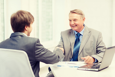 Older man and young man shaking hands while sitting at a desk