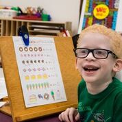 Smiling young boy at school in front of workbook on a stand.