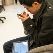 young boy holding iphone close with tablet on his lap