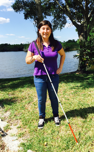 Michelle as a teenager, standing by a lake with white cane