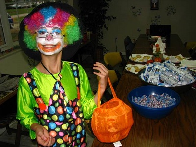 A kid dressed up as a clown for Halloween holding a bag for trick-or-treating