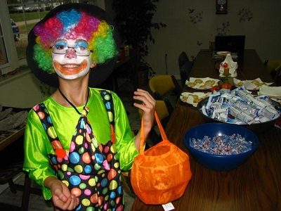A kid dressed up as a clown for Halloween holding a bag for trick-or-treating 