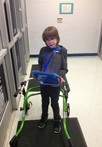 JD Bowdoin standing in front of the school door using his walker