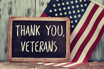 A chalk board with Thank You, Veterans in white chalk in front of an American flag