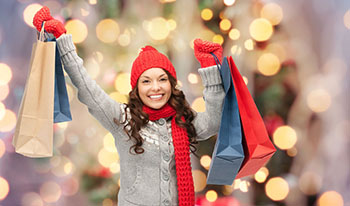 Happy young woman in winter clothes with shopping bags in front of a Christmas tree 