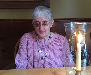 older woman wearing glasses and necklace, seated looking down