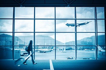 Modern airport scene of a passenger walking inside the airport looking outside through the large window