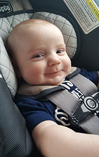 Baby Ben Allen sitting in a car seat smiling at the camera