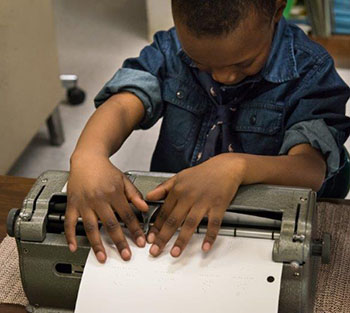 boy leaning over braillewriter