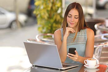 Woman sitting at a table with a laptop looking at her phone