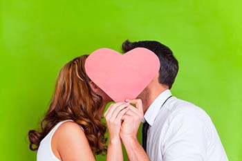 Couple kissing behind a paper pink heart