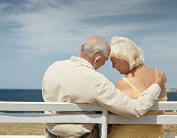 Older man and woman sitting on a bench embracing one another with their backs to the camera