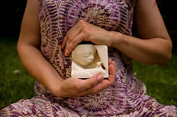 A picture of a woman's torso with her hands in front of her stomach holding a 3D mold of her child's ultrasound