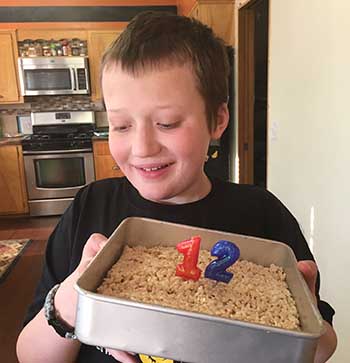 Eddie holding a cake in a pan with two candles on top for this 12th birthday