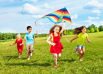 A group of kids running outside flying a kite