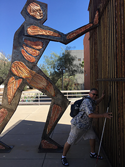 Steven Wilson imitating the pose of a massive sculpture at the University of Arizona called Border Dynamics. The statue appears to be pushing the wall in a lunging position