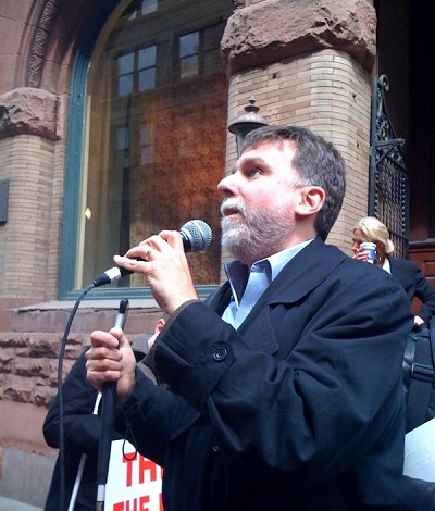 man holding white cane speaking at protest