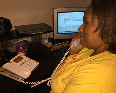 A close up of Empish sitting at her desk in her home office using a landline phone