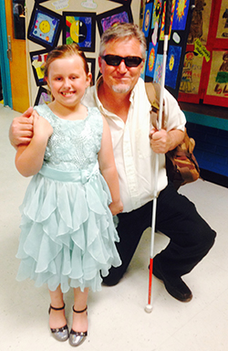 Steven Wilson kneeling next to his daughter Daevi who is in a light blue dress after a school play