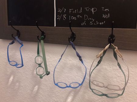 Several pairs of glasses hanging from hooks on a chalkboard