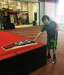 Eddie standing with his white cane touching a large gym mat