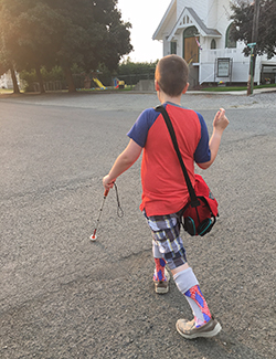 Eddie walking on the street using his long white cane with his back to the camera