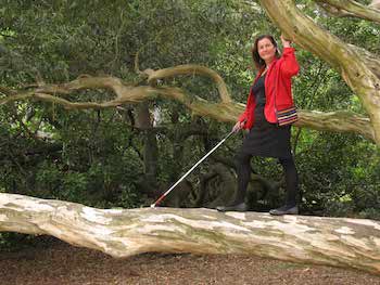 Maribel out on a limb, holding on to a branch and using her long white cane
