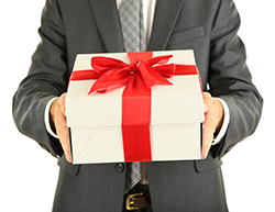 The torso of a man wearing a suit, holding gift wrapped box with a big red ribbon