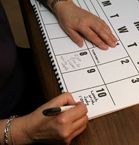 person writing on large print desk calendar