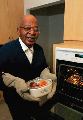 Older man standing by an oven, using oven gloves to hold a casserole dish.