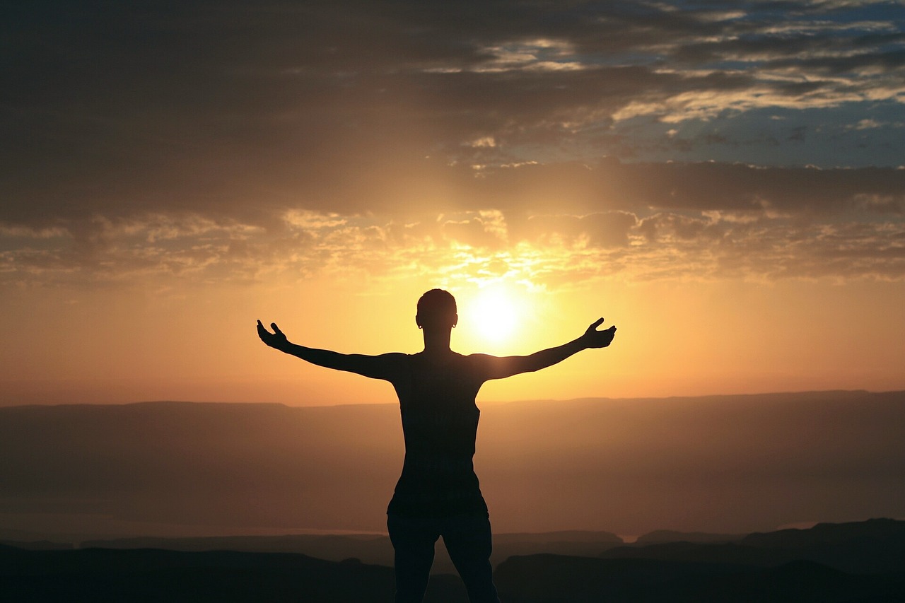 Silhouette of woman standing with arms outstretched facing morning sunrise