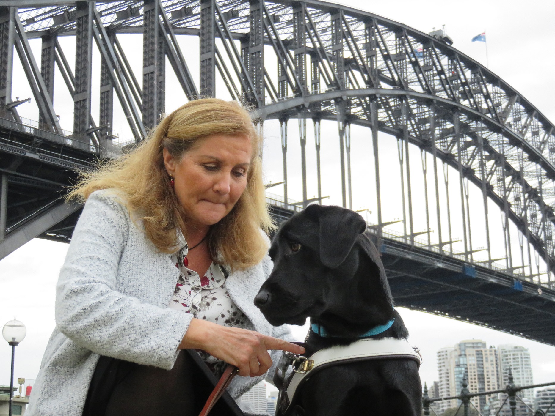 Maribel and black lab guide dog in front of Sydney Bridge