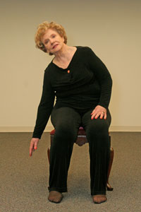 seated older woman bending to her right with right arm pointed straight to the ground