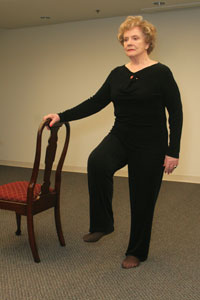 a woman holding on to a chair on her right side while she 

raises her right foot off the ground