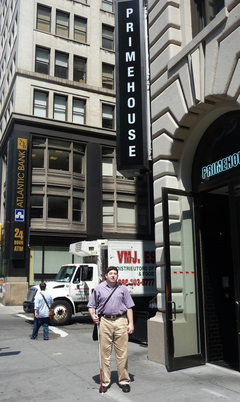 Daniel standing on the corner of Park Avenue and 27th Street, holding his cane, beneath the vertical, two-story Primehouse sign