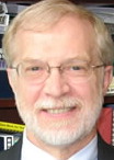 A head shot of Dr. John Crews. He is in his office, standing in front of a bookcase as a backdrop.